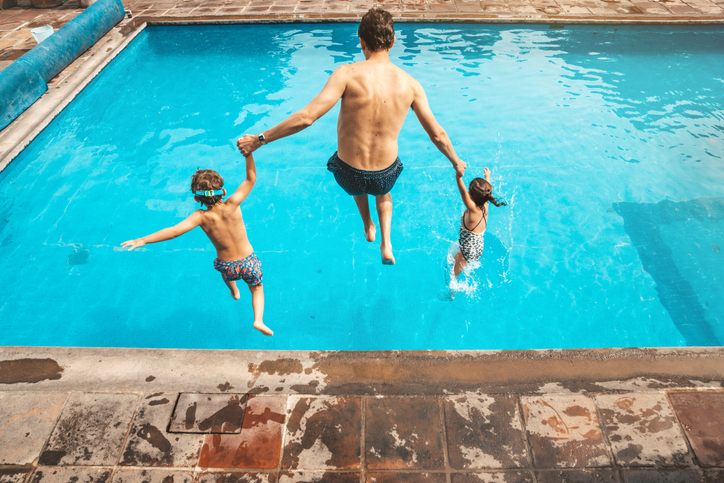 father and two children jumping into pool