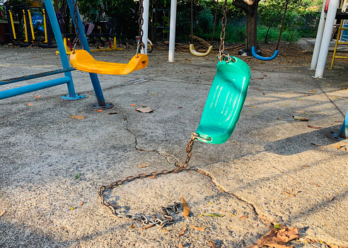 Broken swing dangling from one chain in a playground.