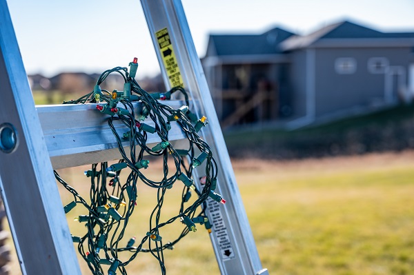 Prep for installing Christmas lights by leaning a ladder against a house and setting out lights